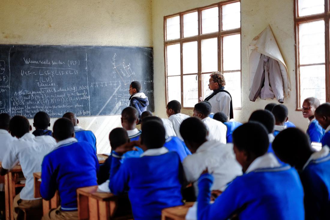 A female teacher and classroom pay attention to one student at a chalkboard in front of the room in Rwanda