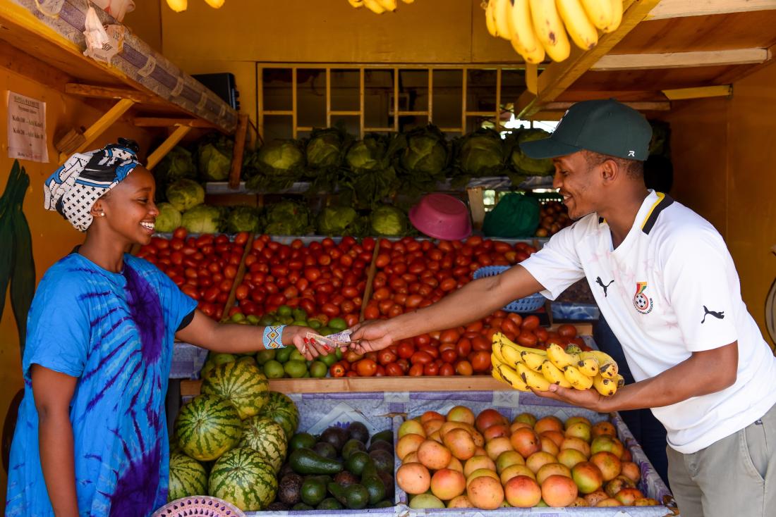 A sales transaction for a banana bunch is seen with man exchanging change with vendor at fruit stand in Kenya
