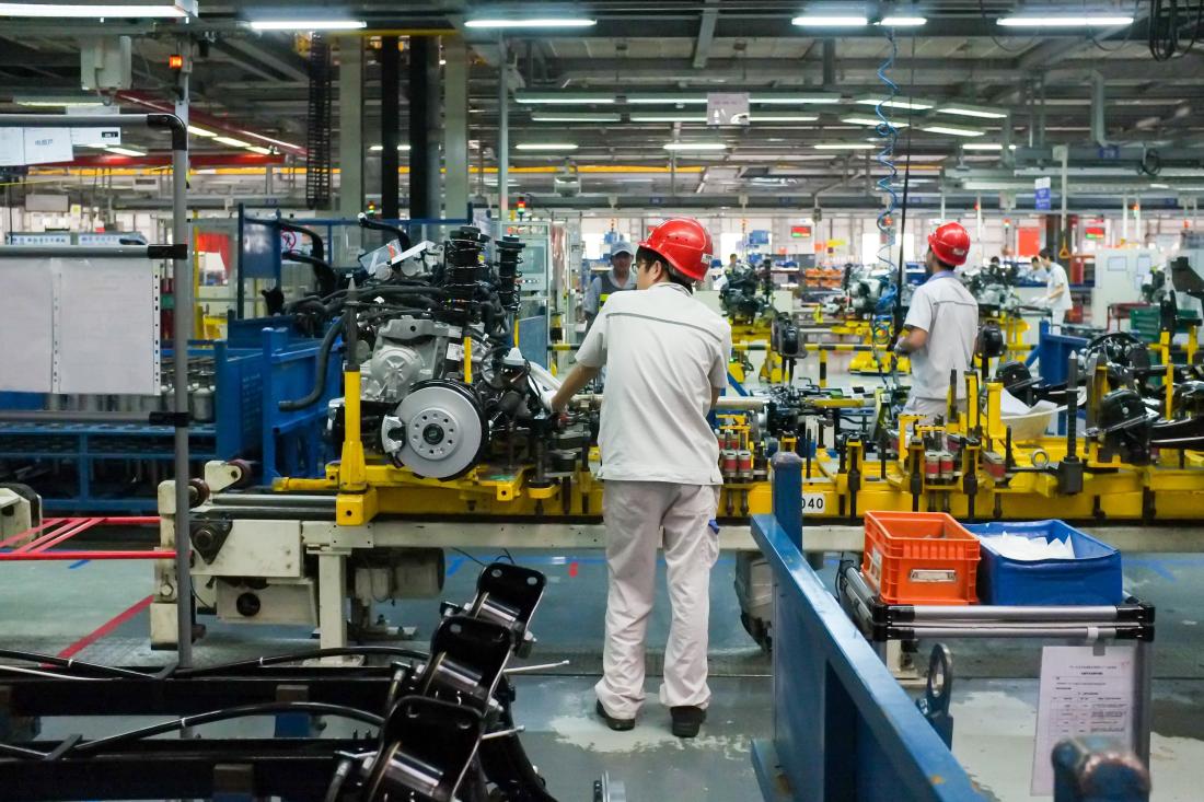 Worker wearing a red hard hat monitoring machinery at a car assembly factory in China