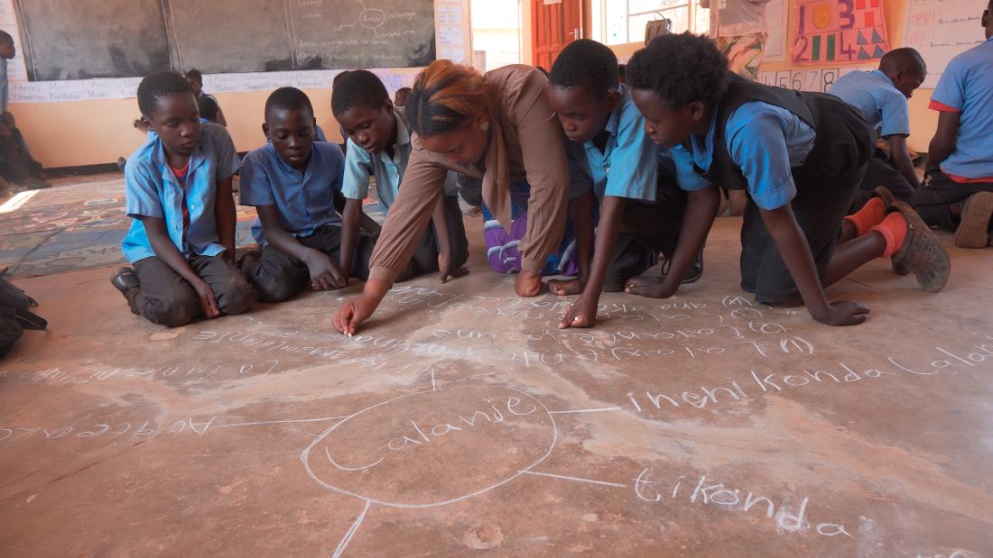 Students squat and write math problems using chalk.