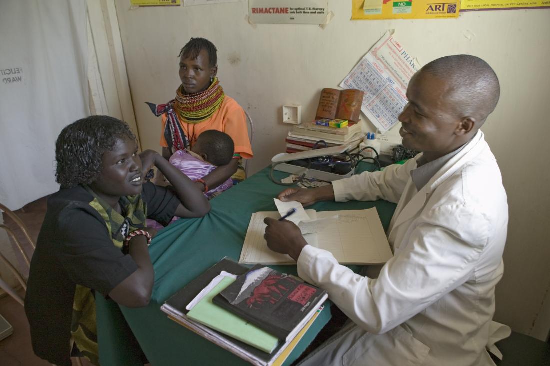 A doctor talks to a patient at a desk.