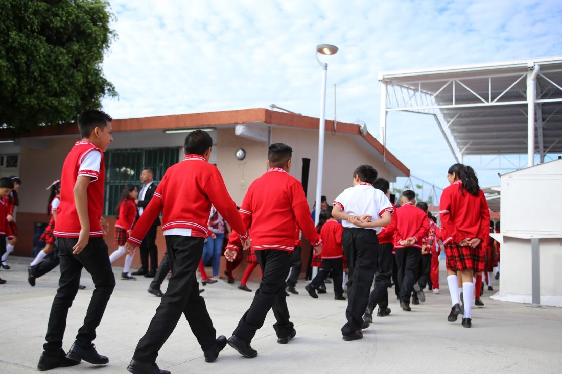 A line of students wearing red school uniforms walks to a school assembly