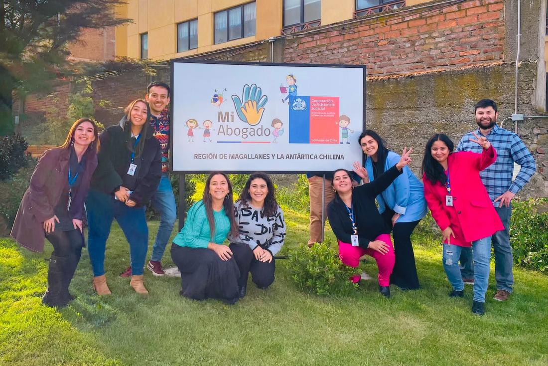 Members of the Mi Abogado program team in Magallanes, Chile, pose outdoors beside a large sign displaying the Mi Abogado logo and the Chilean Ministry of Justice and Human Rights.