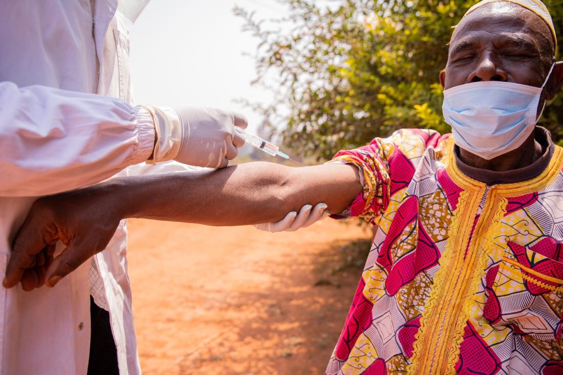 A man wearing a surgical mask receives a vaccination in his left arm.