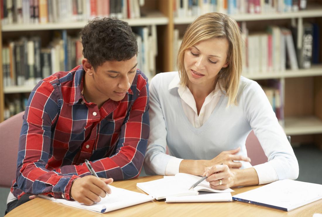 Woman and young man look at homework in a library