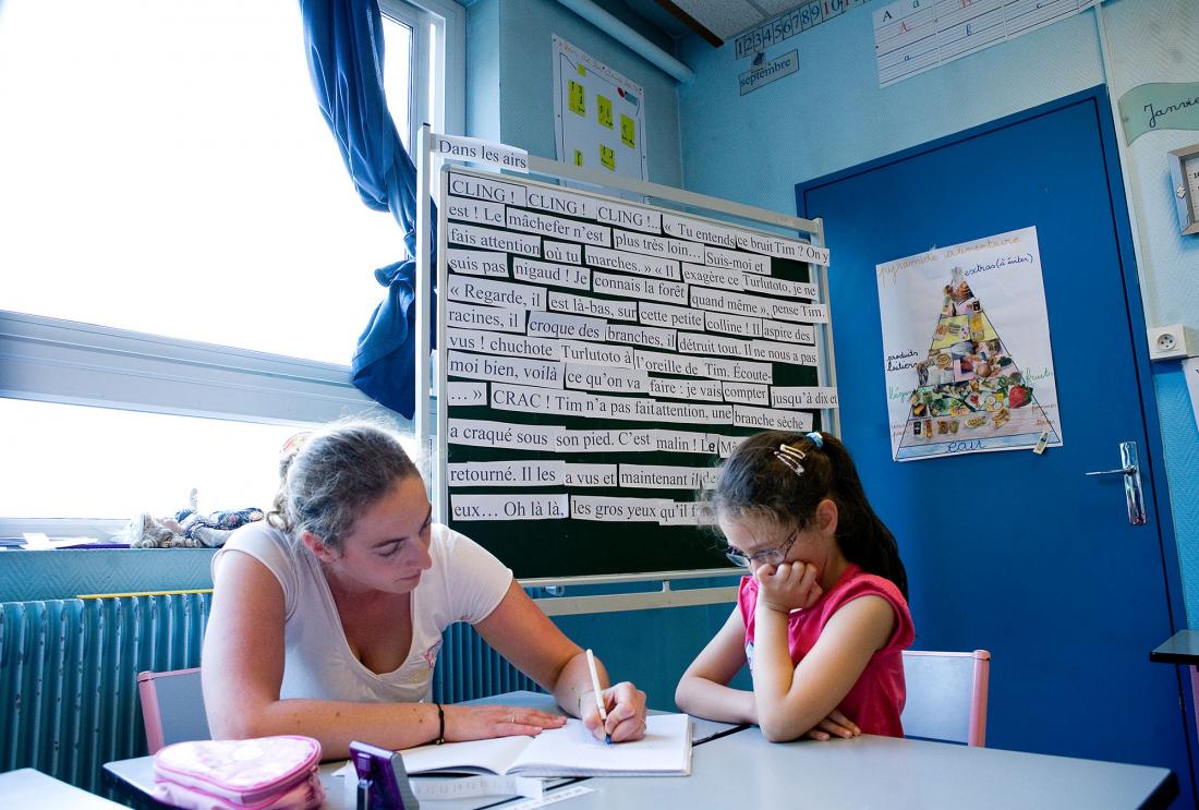 Adult and child sit in classroom looking over papers