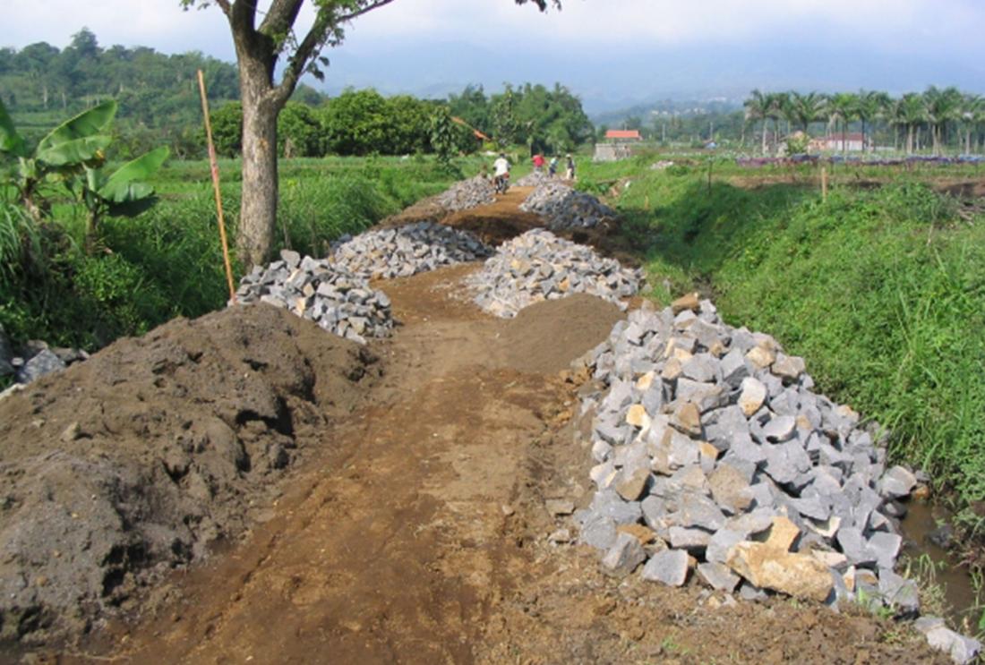 Dirt road in rural area with piles of rocks along edges