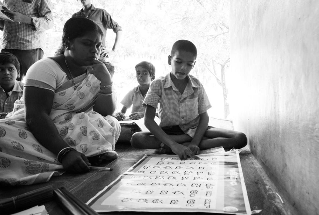 Child sits and reads while woman looks on