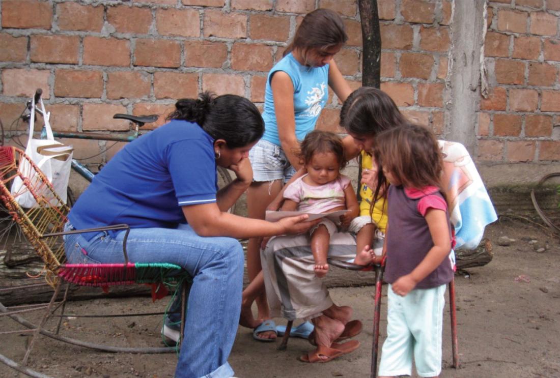 Two adult women sitting in chairs reading with three children.