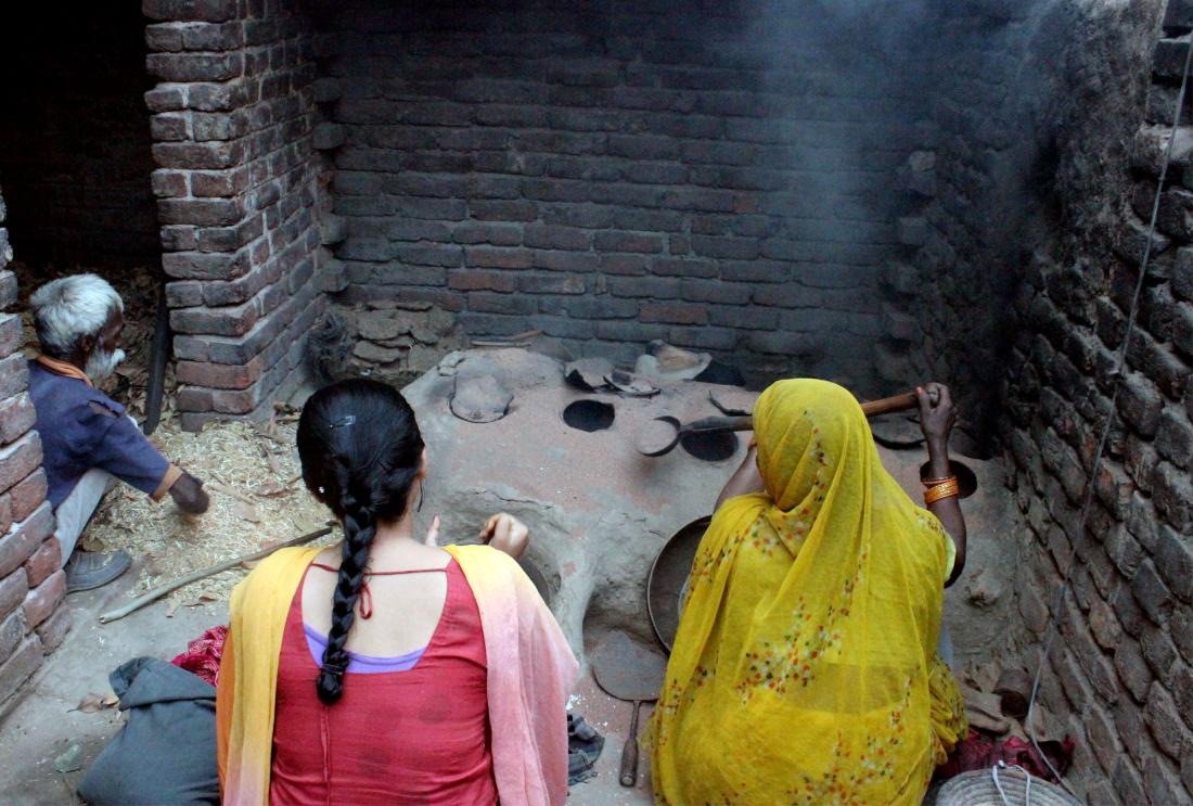 Two women sit in front of mud stove