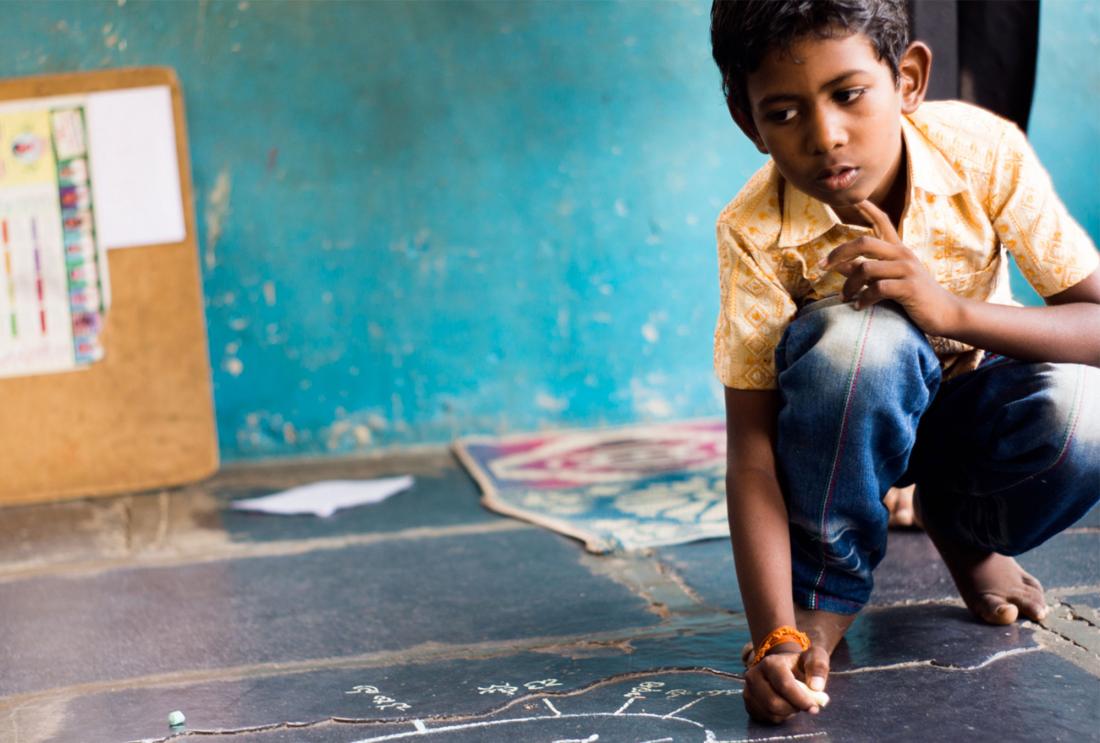 Young boy pauses in thought while writing on the floor in chalk