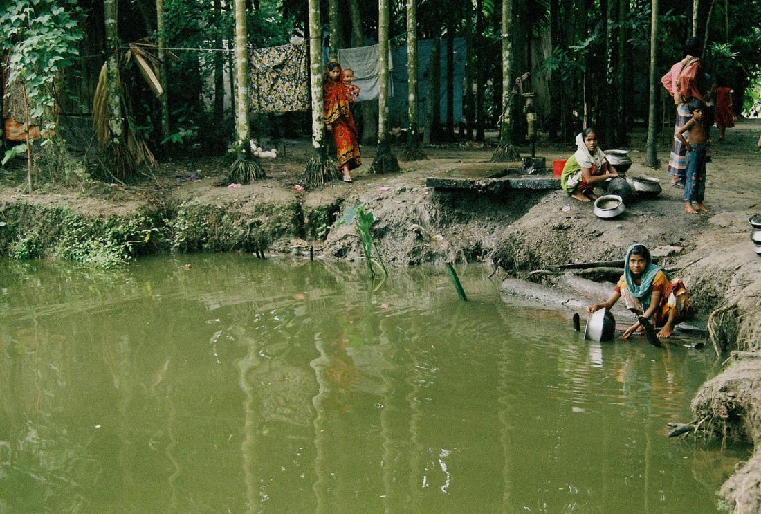 Women gather around pond with well pump