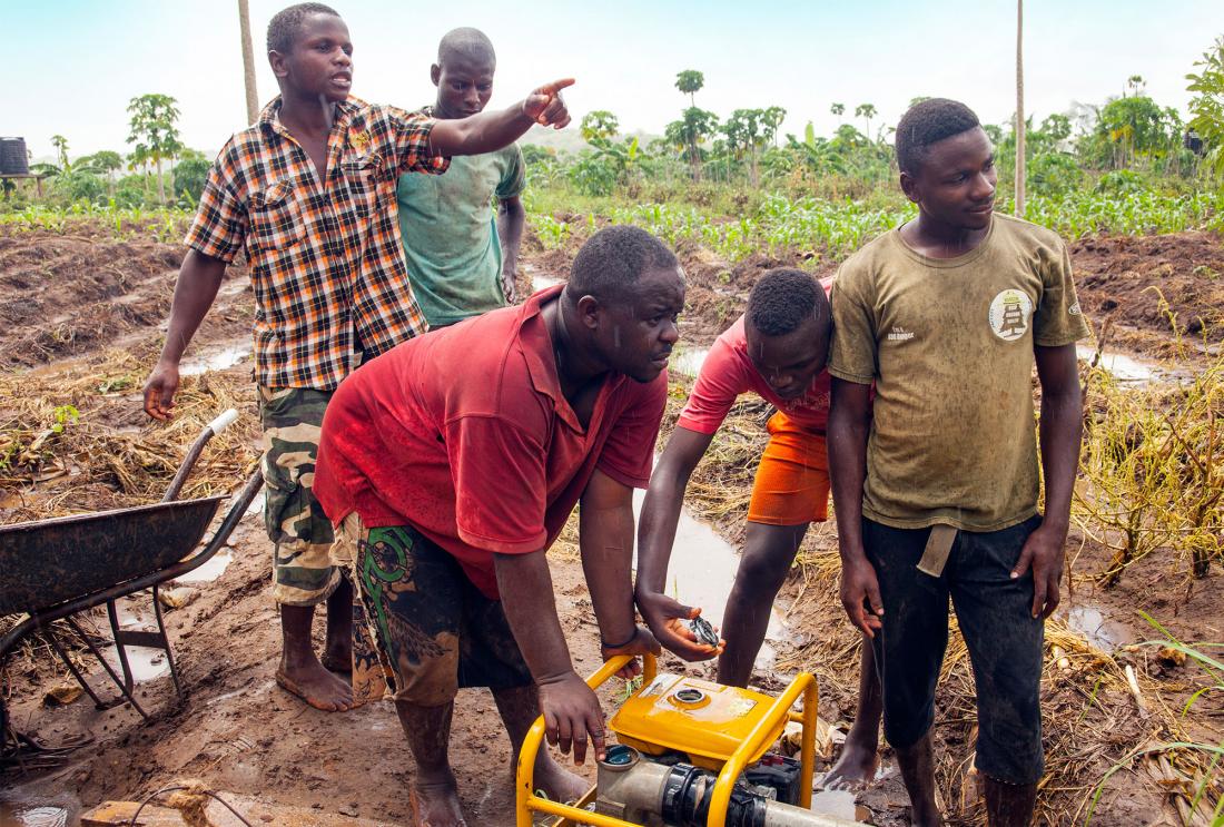 Five men stand in a field in the rain operating a small pump machine