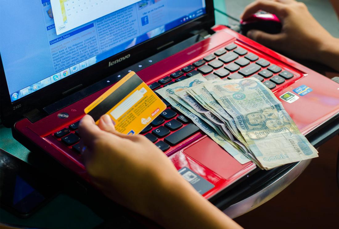 Person works on laptop with Philippine currency and bank card