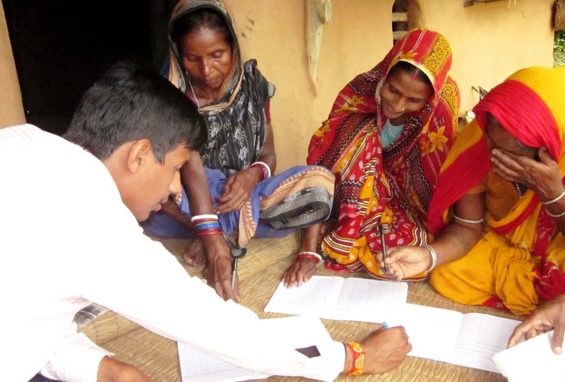 Three women in saris look at paperwork with Bandhan staff