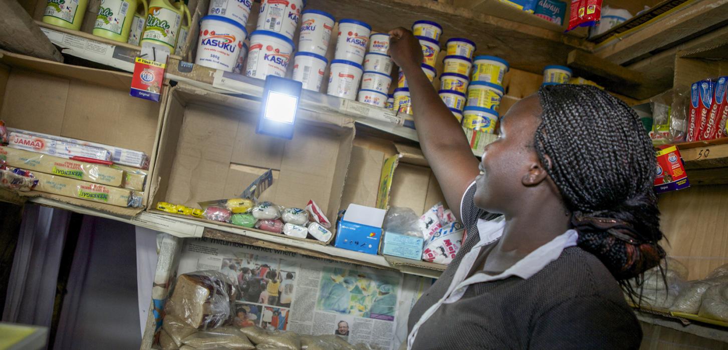 A woman reaches for a can on a shelf.