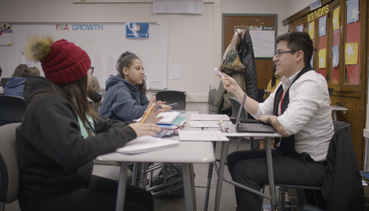 Two high school students sit at desks with their tutor for personalized instruction