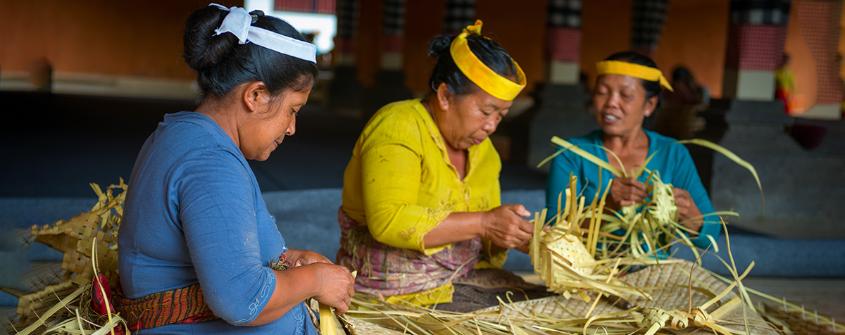 Women make baskets for balinese traditional offerings to gods in temple 