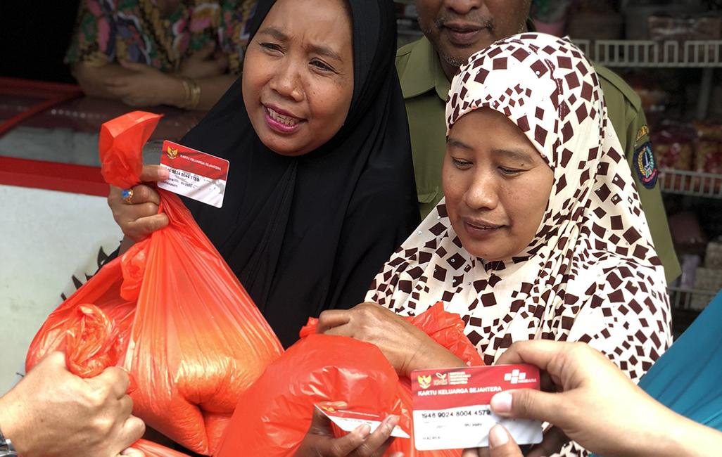 Two women holding bags of rice with their non-cash food assistance cards.