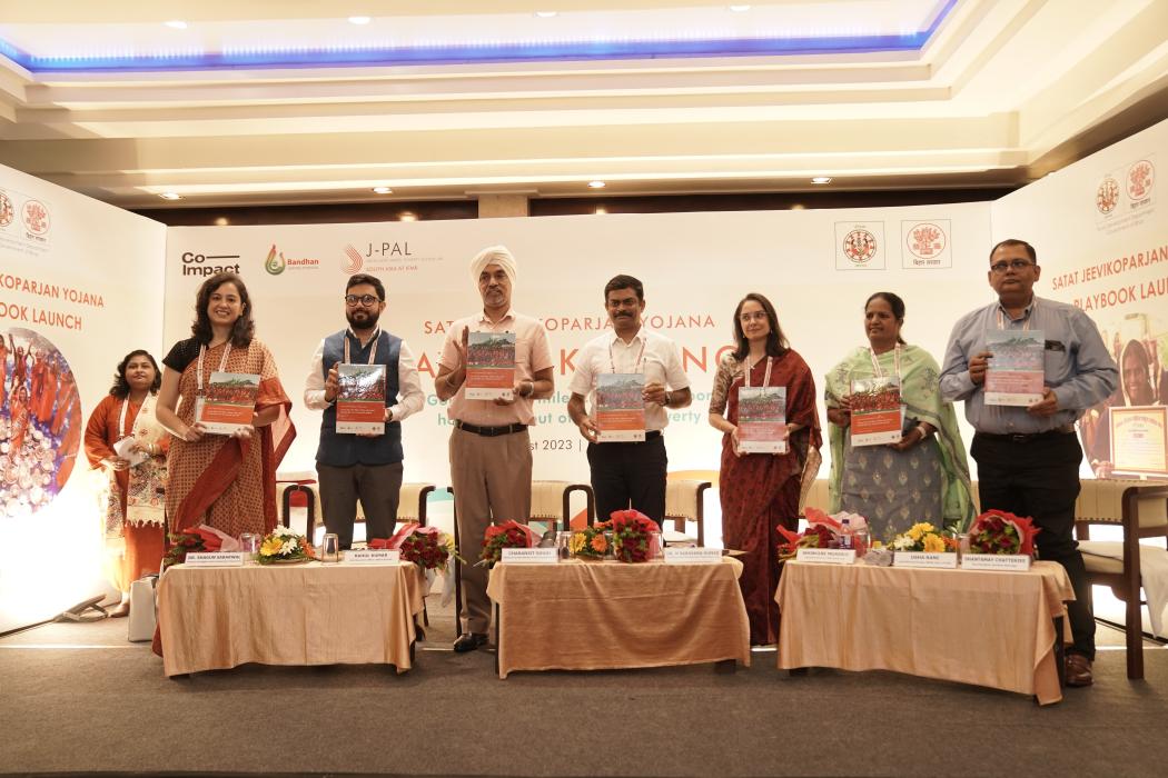 A group of government officials, partners, and J-PAL South Asia team members stand on stage holding up copies of the Satat Jeevikoparjan Yojana Playbook during its official launch event in Bihar.