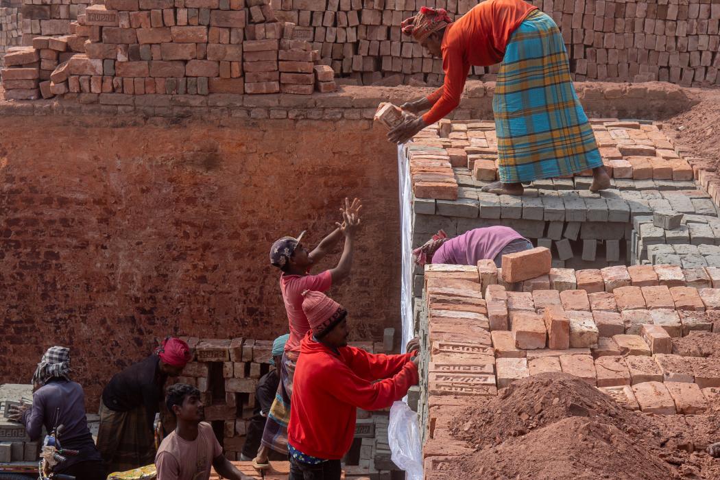 Multiple kiln workers stack bricks outside.