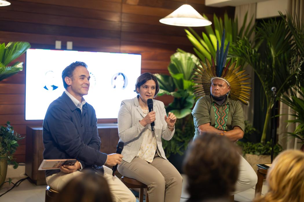 Esther Duflo speaking in the middle of two men on stage