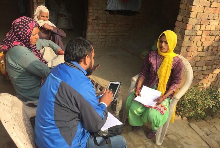 A person with a tablet speaks to a person holding a paper.