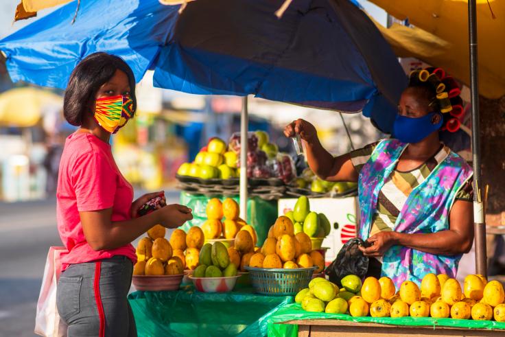 Two women making buying and selling produce at a local market during Covid-19