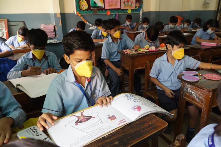 Masked students sit at desks in a classroom.