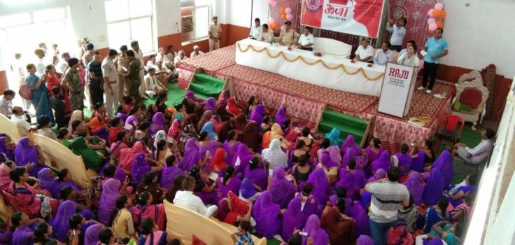 A large group of mostly women, many of whom are wearing purple, sits in front of a stage with eight people on it.