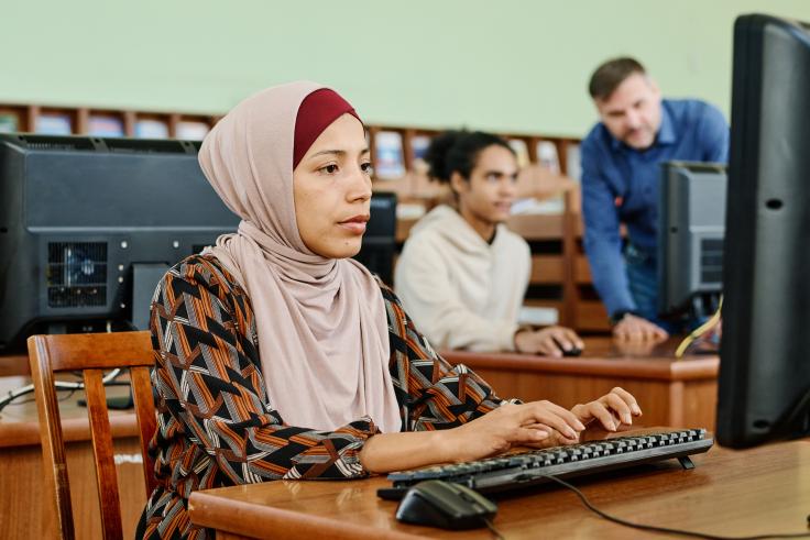 Young woman sitting at a computer working with two people in the background