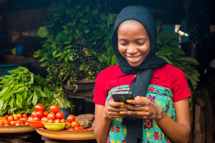 Young woman smiles while holding a cell phone in front of a market
