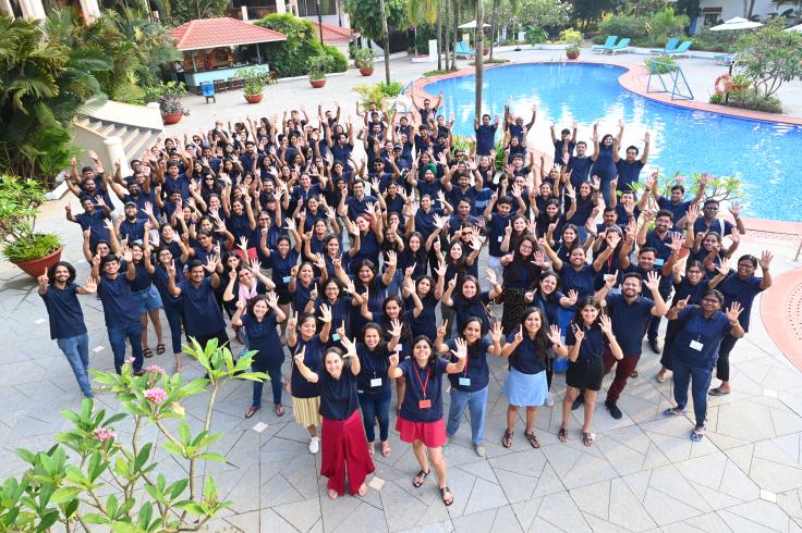 Large group of J-PAL South Asia staff standing with hands raised next to pool at a resort