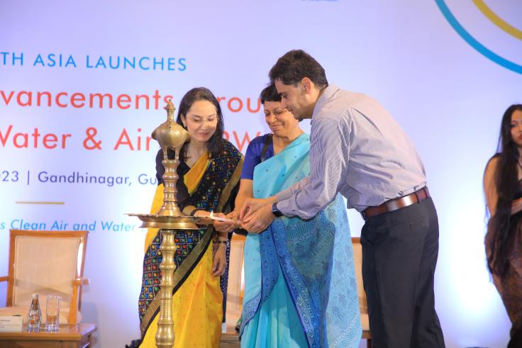 Three people light a lamp on a stage.