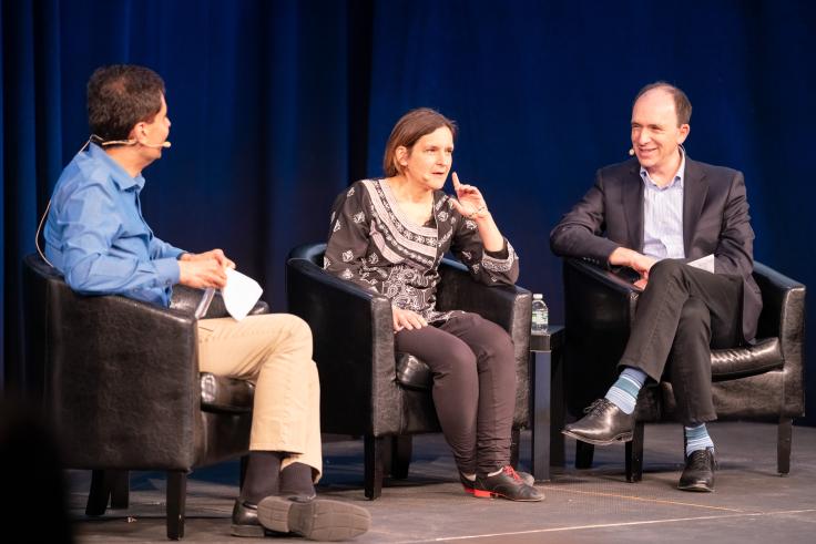 Two men and a women are seated on a stage.