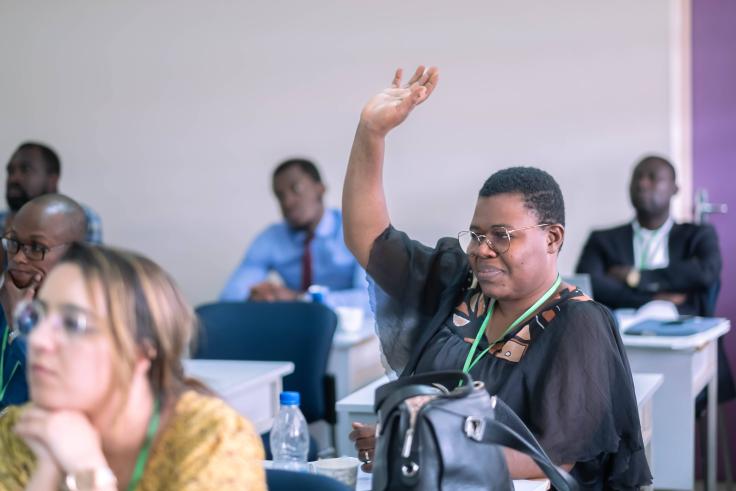 Classroom of attentive students with woman in middle raising a hand.