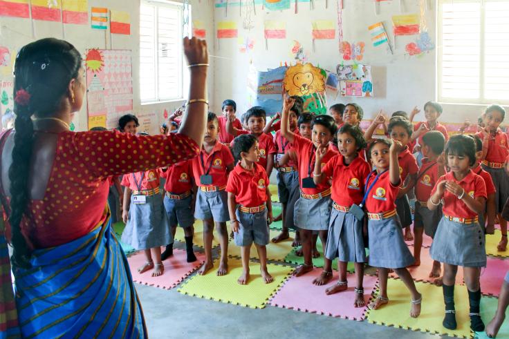 Teacher with a raised hand standing in front a group of elementary students 
