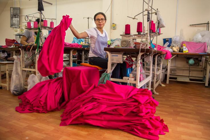 Woman placing a sewn skirt on the ground while sitting at her sewing machine