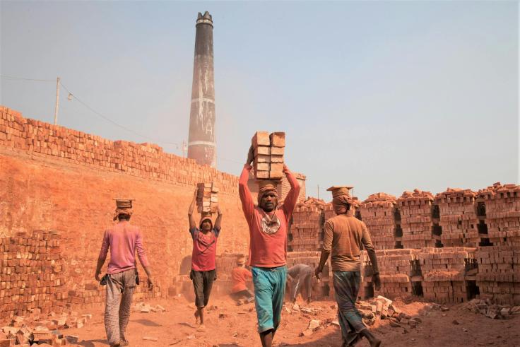 Four men walking with bricks on their heads in a brick manufacturing plant