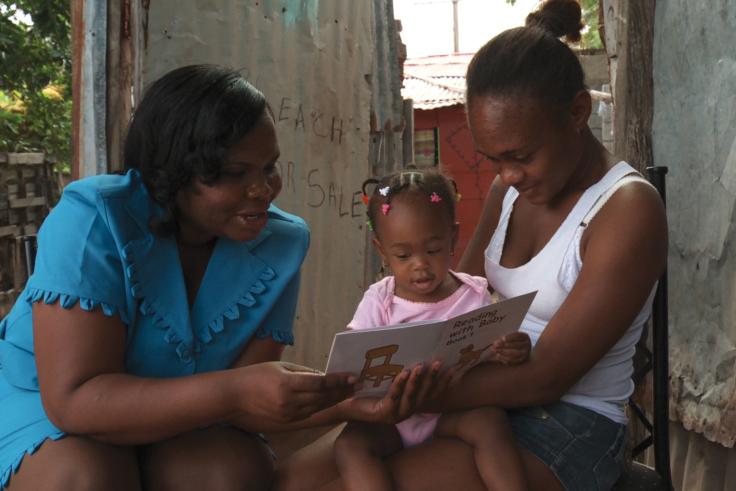 Facilitator sitting with a mother and young child reading