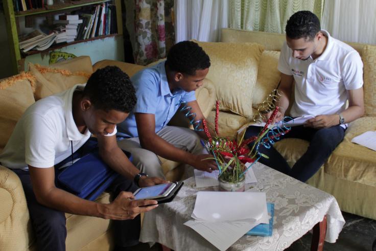 Two teenaged students review a tablet with a facilitator while sitting on a couch