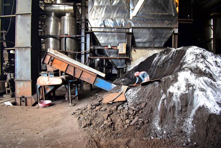 Man standing in a pile of soot at a factory shoveling 