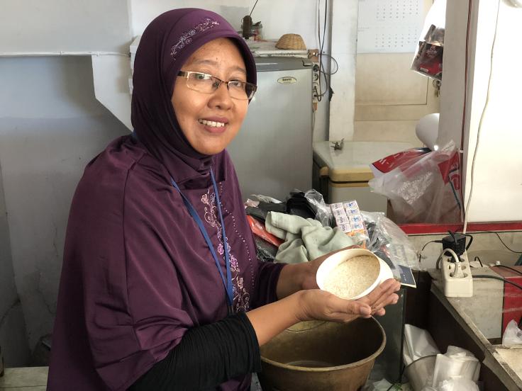 A woman smiles while holding a bowl of uncooked rice.
