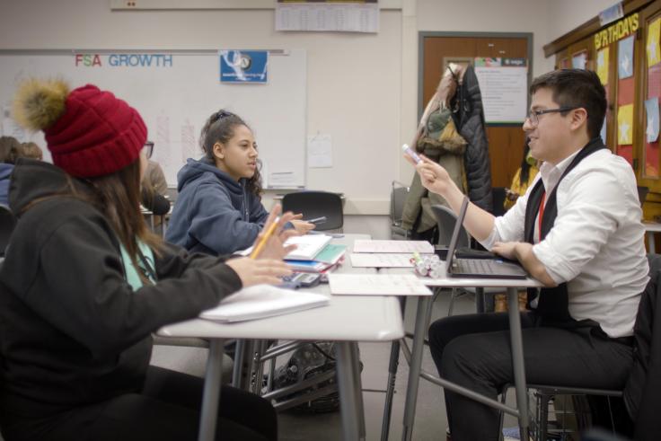 A tutor holding a marker sits across from two female