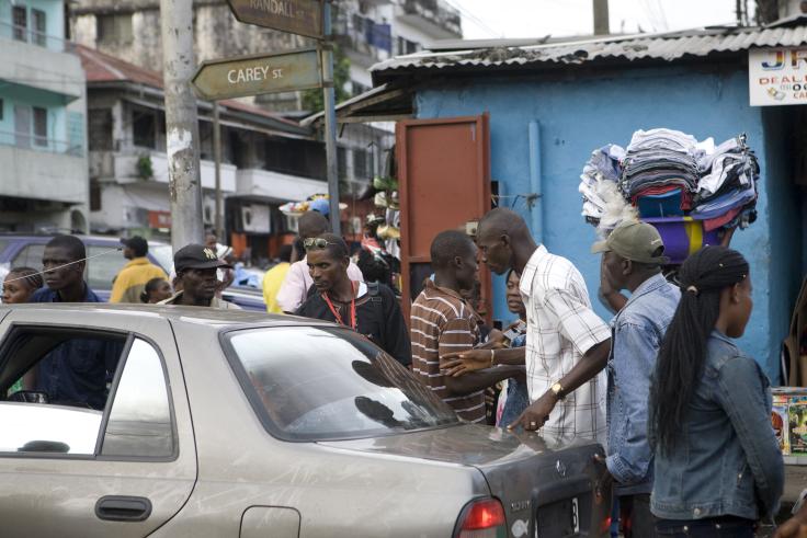 Men and woman walking through a busy street next to a car