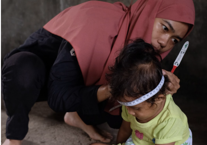 A woman measures a baby's head with a measuring tape