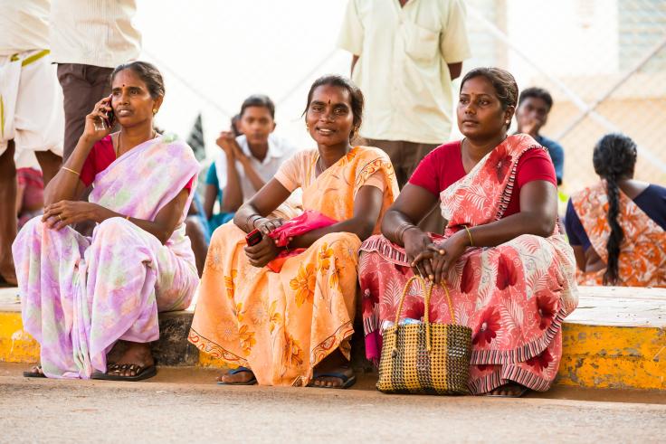 Three women in bright clothing sit down a look out onto the street