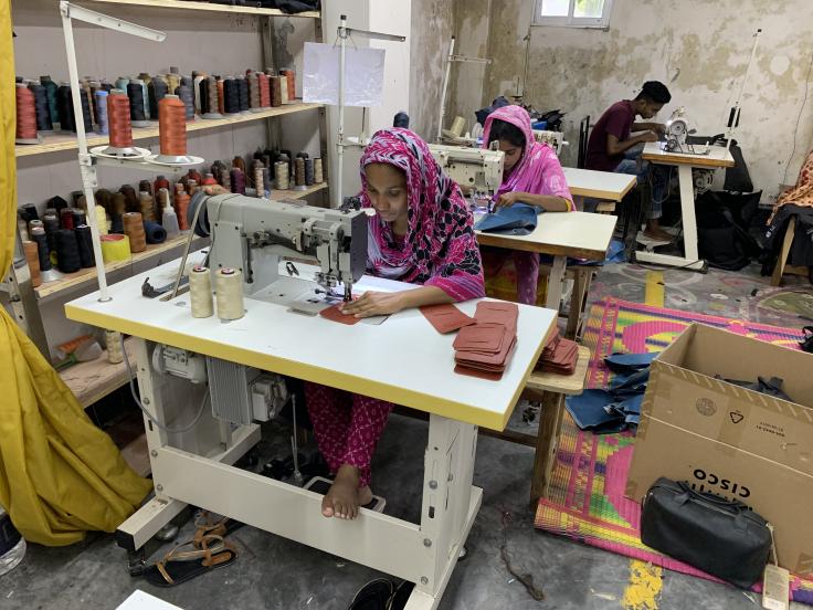 A woman sits at a sewing machine making textiles.