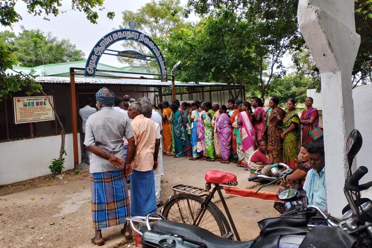 Men and women stand in line outside of a government health facility