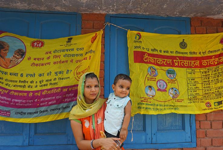 Woman holds child in front of immunization poster